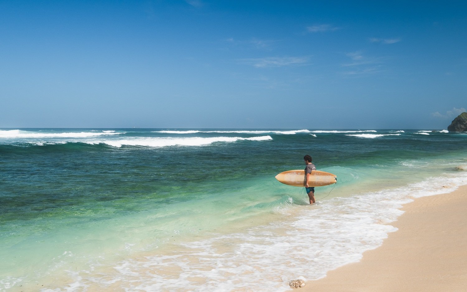 A surfer standing in the water looking out at the waves in Uluwatu, Bali