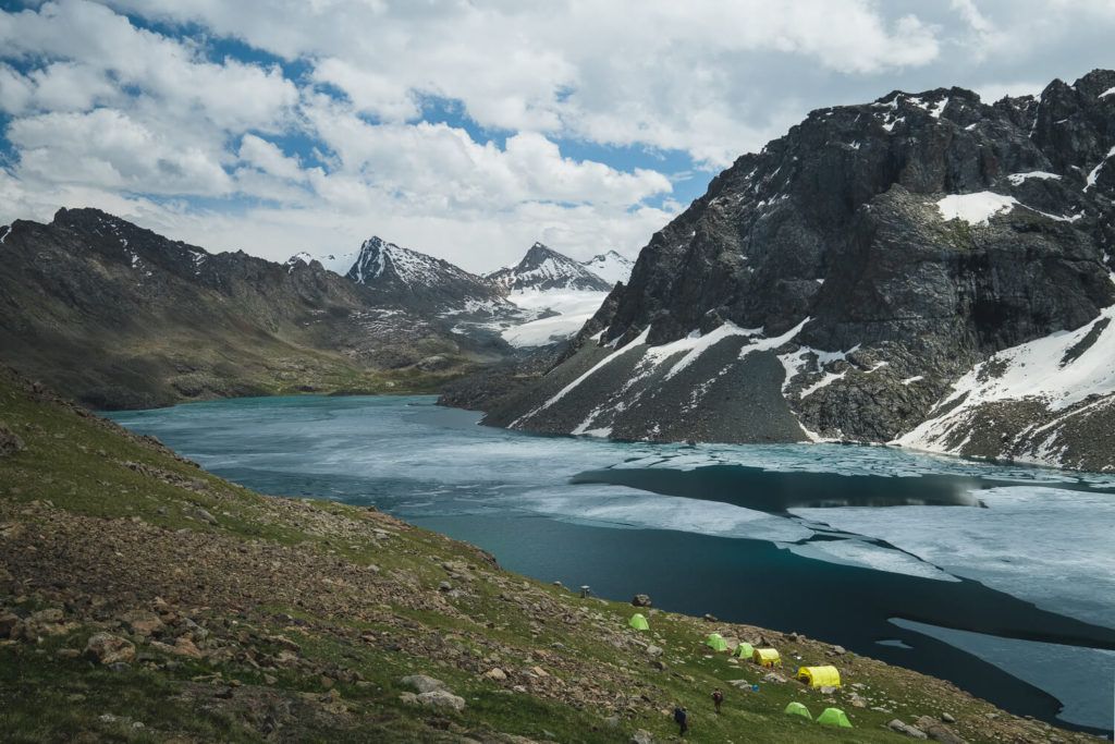 A glacial river flowing down a valley next to some large mountains in kyrgyzstan with some tents by the side of the river camping