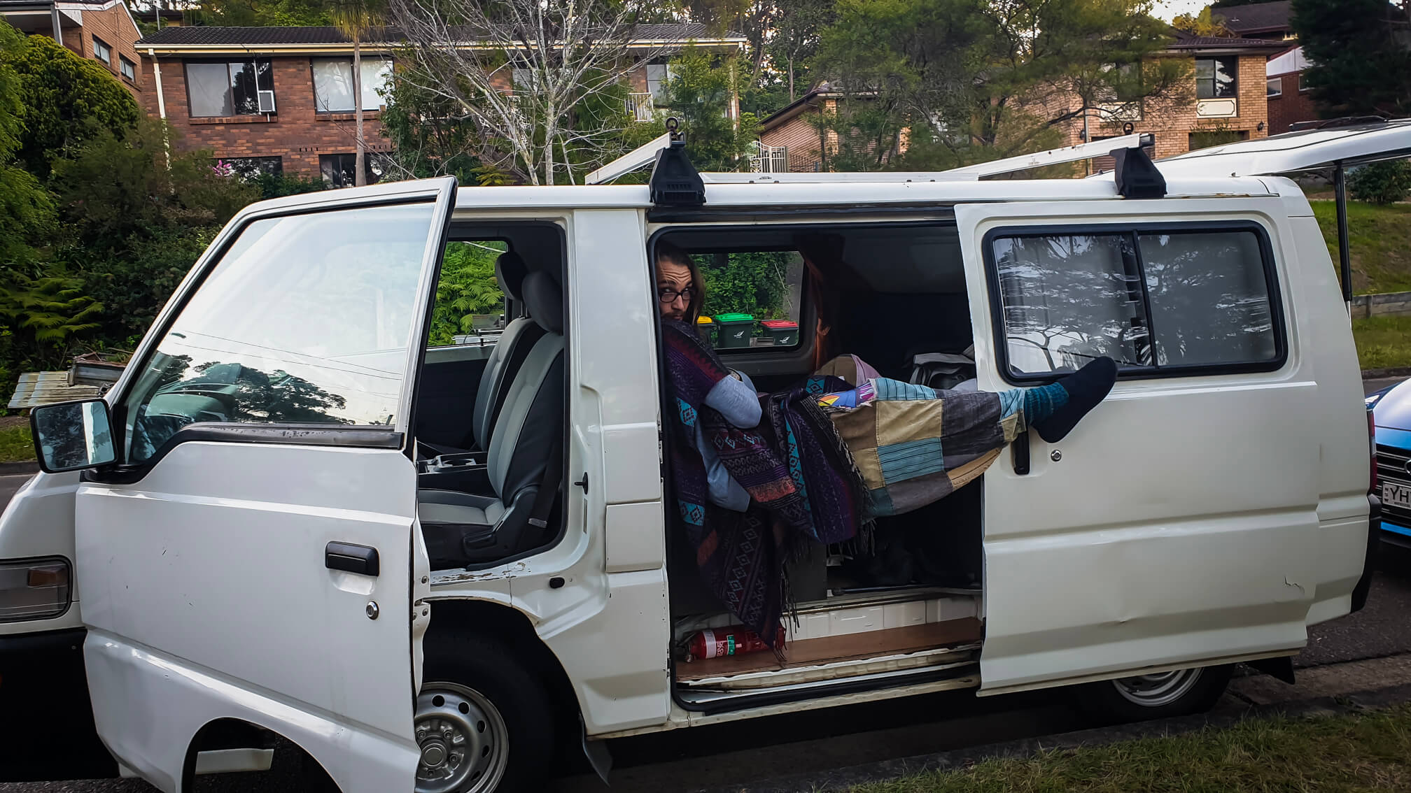 man sitting in an old white converted campervan while travelling overland