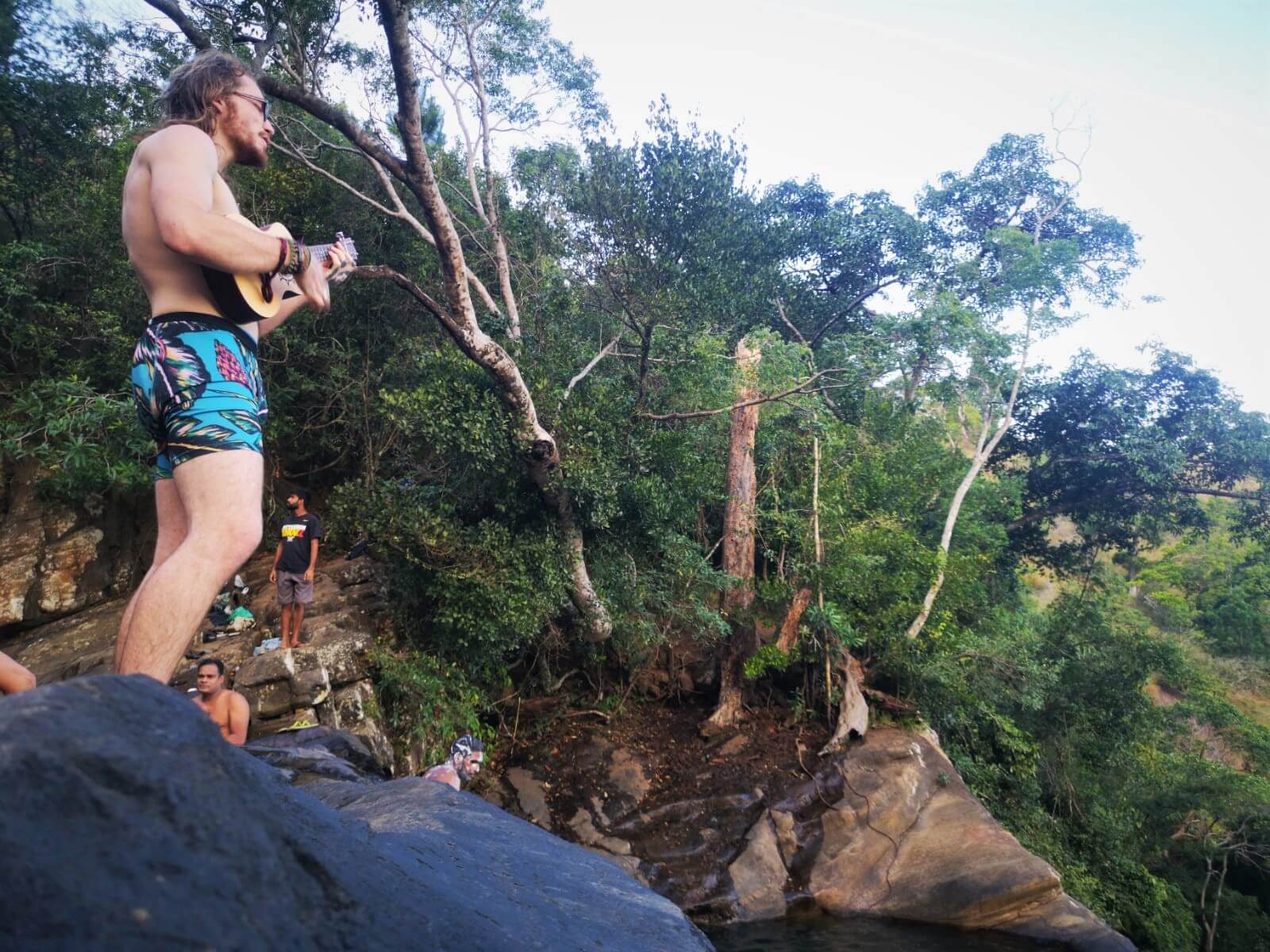 A budget backpacker in Sri Lanka playing ukulele at a famous waterfall