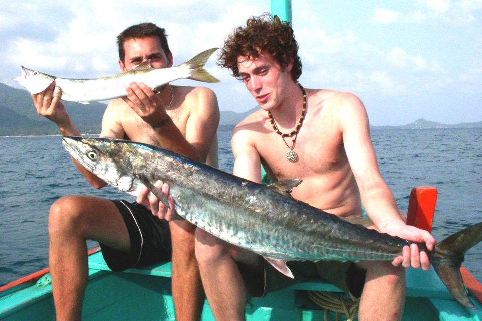 Two guys hold up their fish on the pacific. 