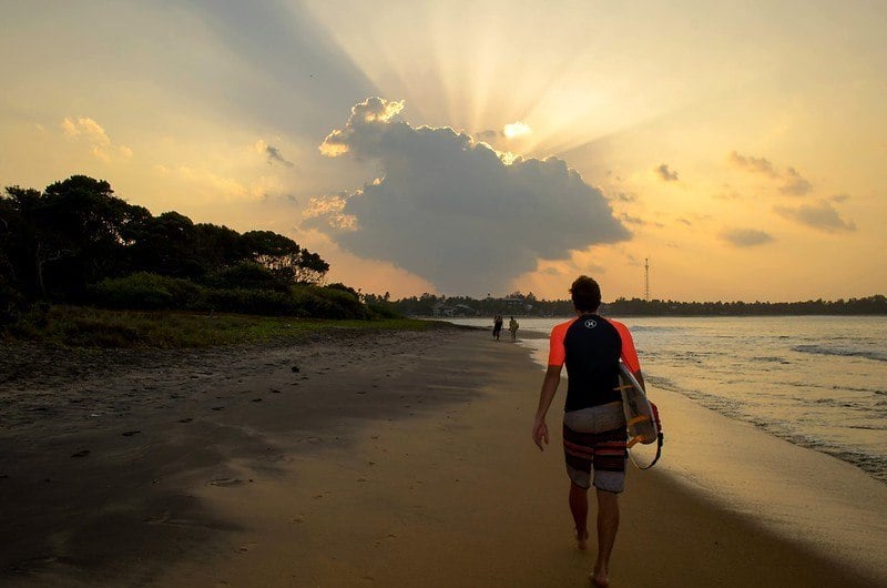 Man surfing in Arugam Bay walks down a sunset beach