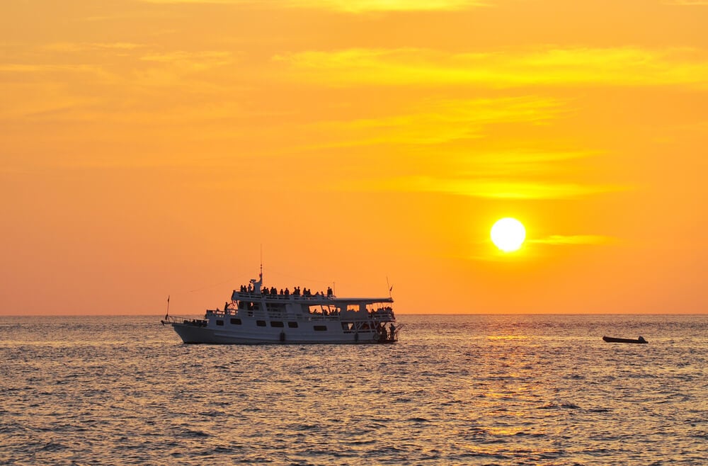 sunsetting over the sea whith a boat cruising along in front