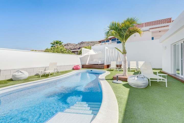 Outdoor pool area with palm tree, sun loungers and bean bags around