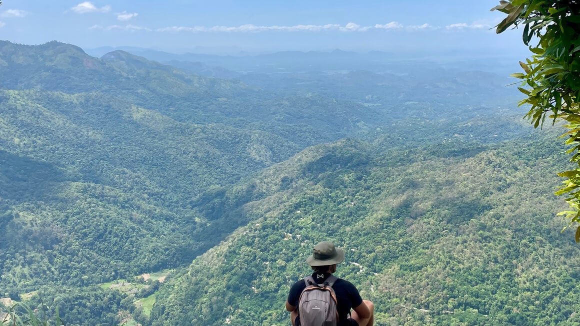 harvey sitting on a rock at the top of ella rock looking over mountains, sri lanka