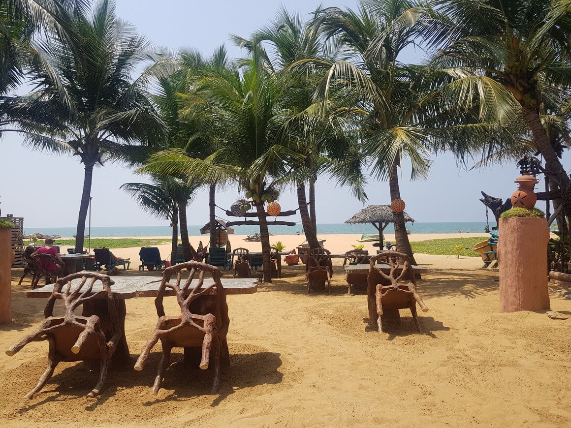 wooden tables and chairs laid out in front of palm trees on the sand of the beach
