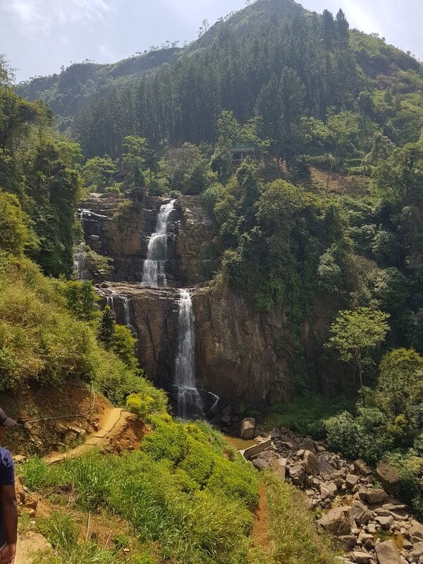 waterfall over green covered orange cliff rocks on a sunny day