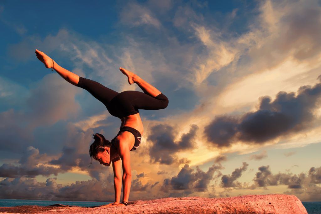 A woman backpacking cambodia practises yoga handstands at the beach