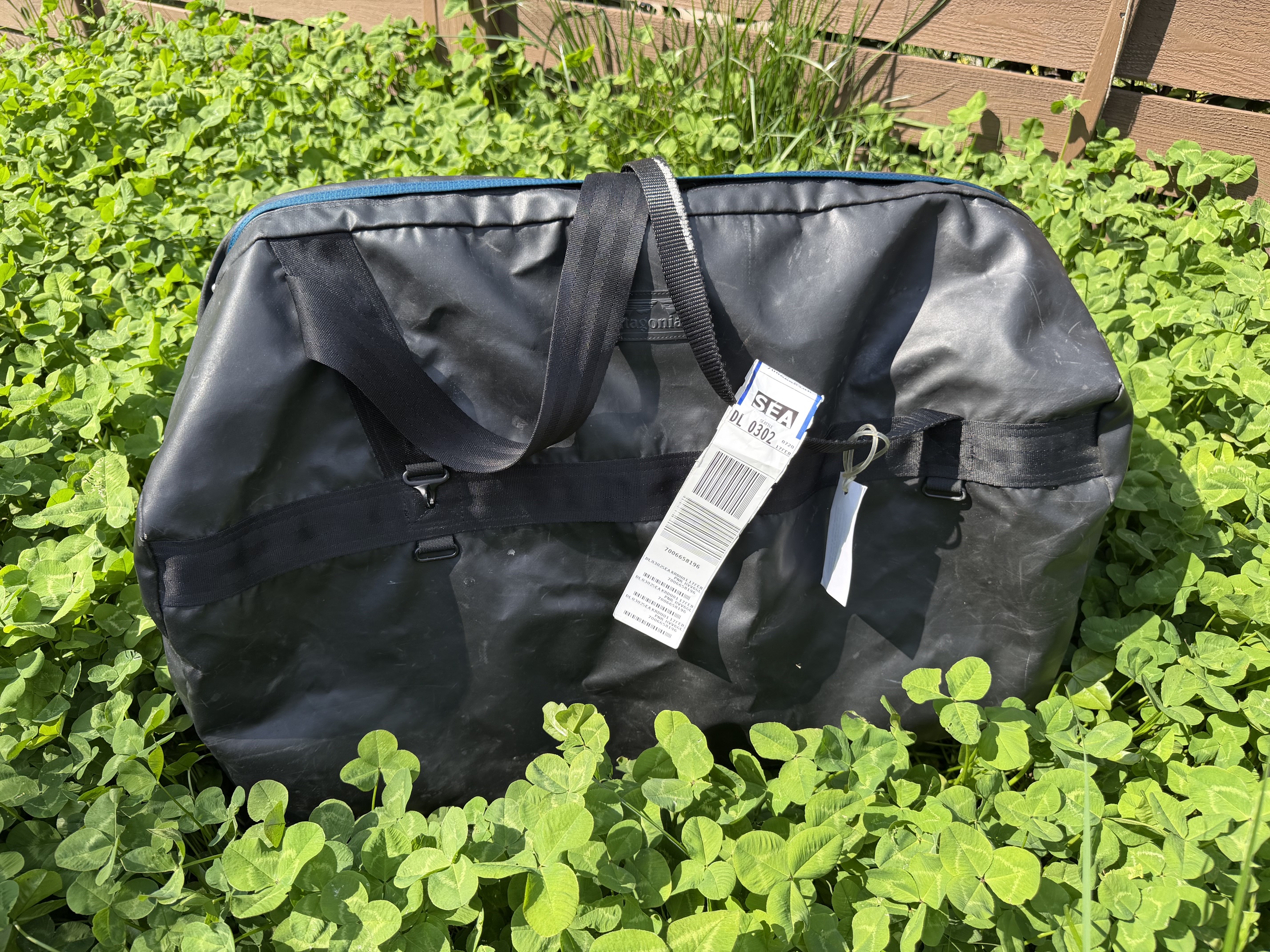 Beat up Patagonia Black Hole duffle bag sitting in some clover with an airline tag on it
