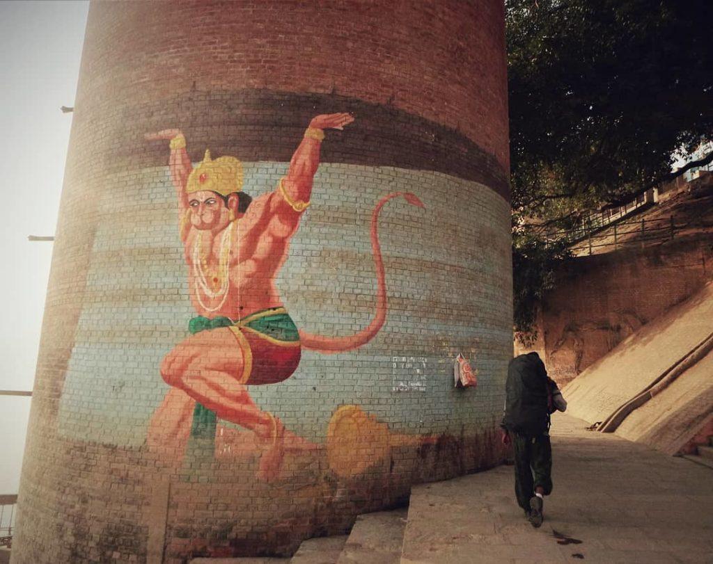 A budget traveller in India walking past a Hanuman mural with his backpack
