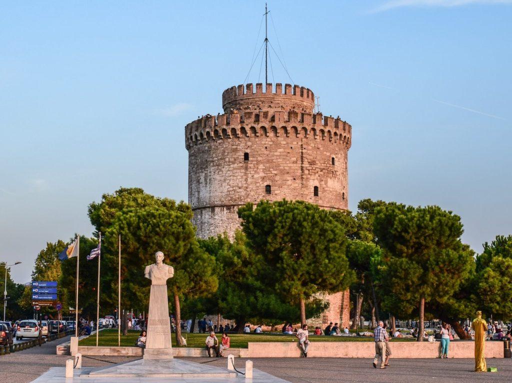 A statue of a man in front of the White tower of Thessaloniki, in Greece