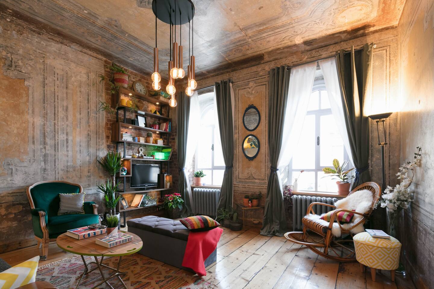 19th Century, wooden living room with large windows, comfy chairs and a book case.