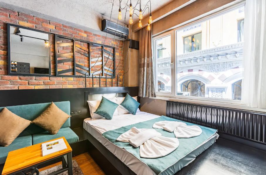 Industrial designed, modern bedroom with large window and leafy green coloured sheets.