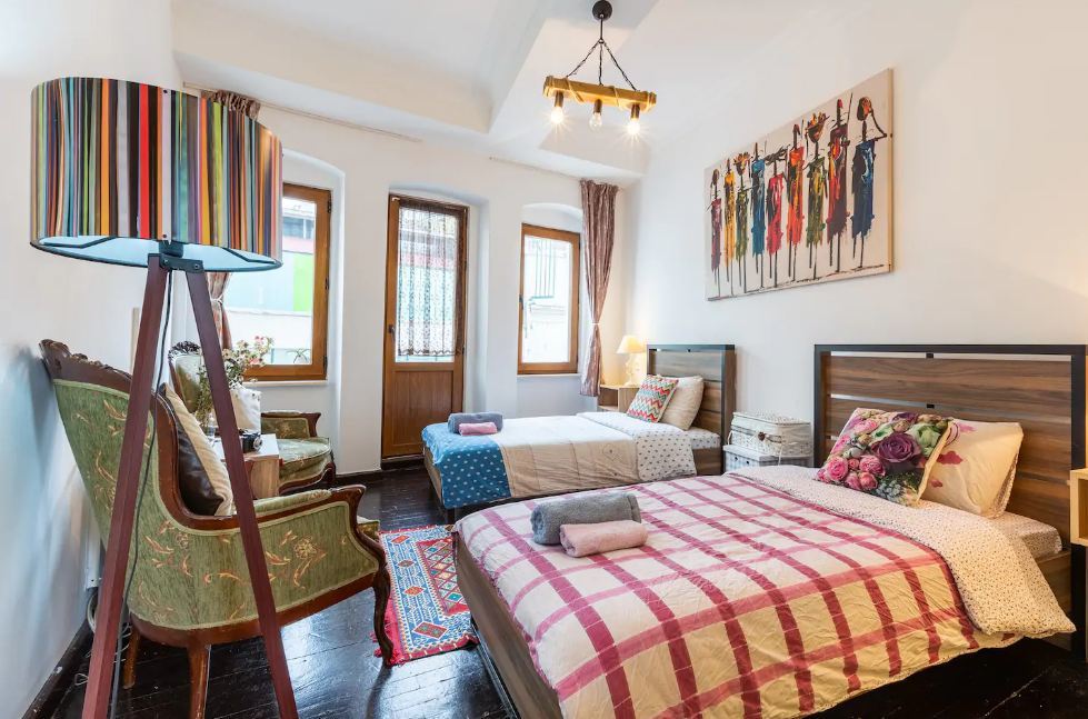 Colourful but simple twin bedroom with two arm chairs, a lamp and art on the wall.