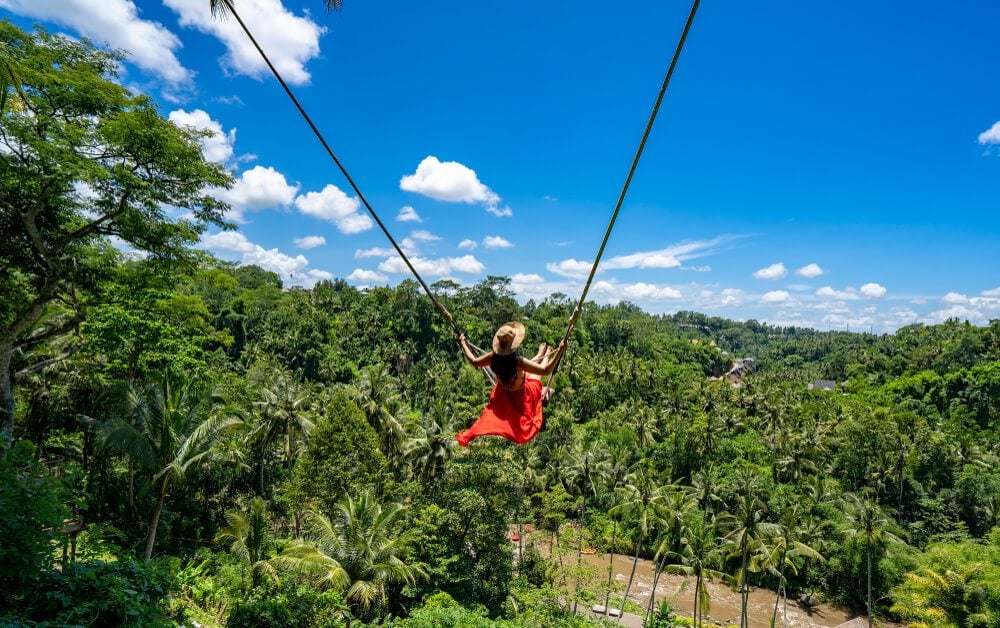 woman swinging in the middle of a rice field while staying in ubud