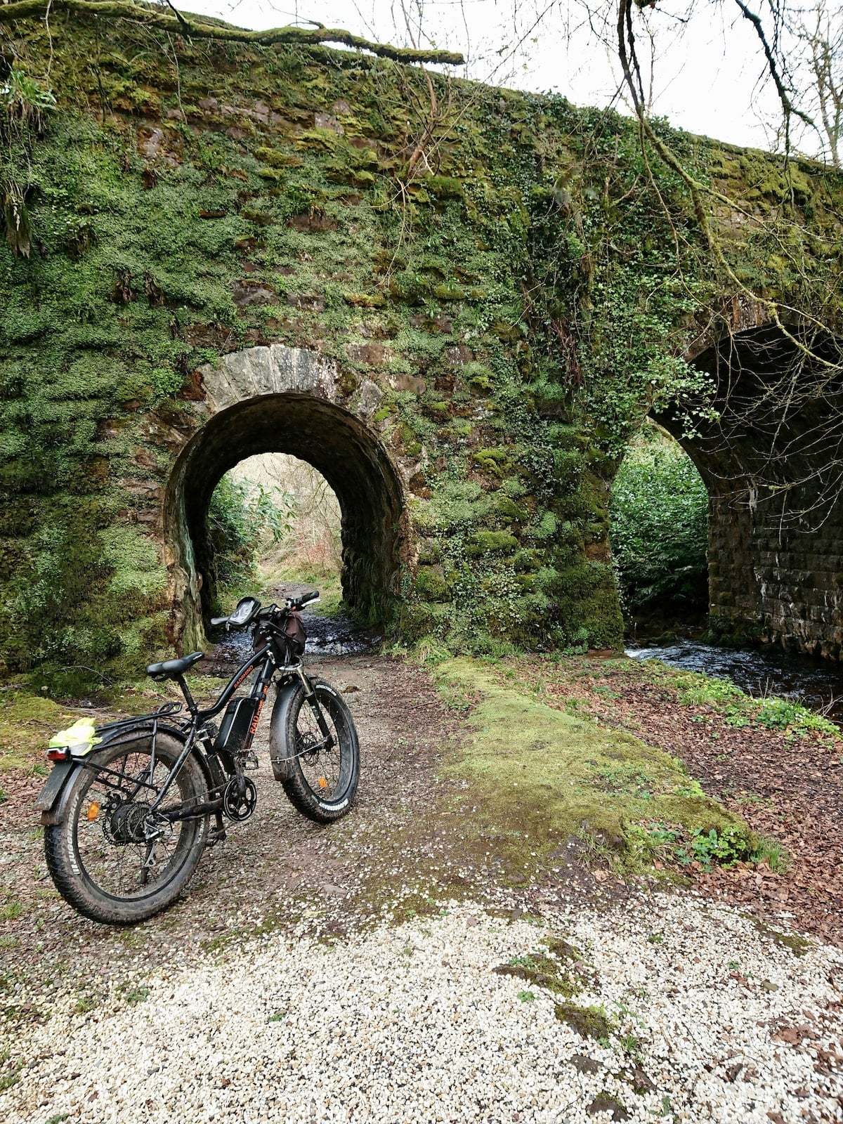 A black bicycle parked on a dirt path near a stone bridge in Galway