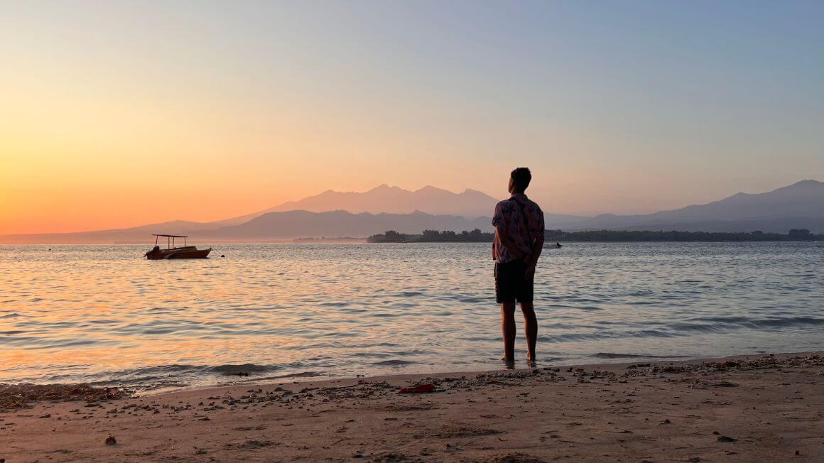 a man stands near the water on the beach watching the sunset at gili air, indonesia