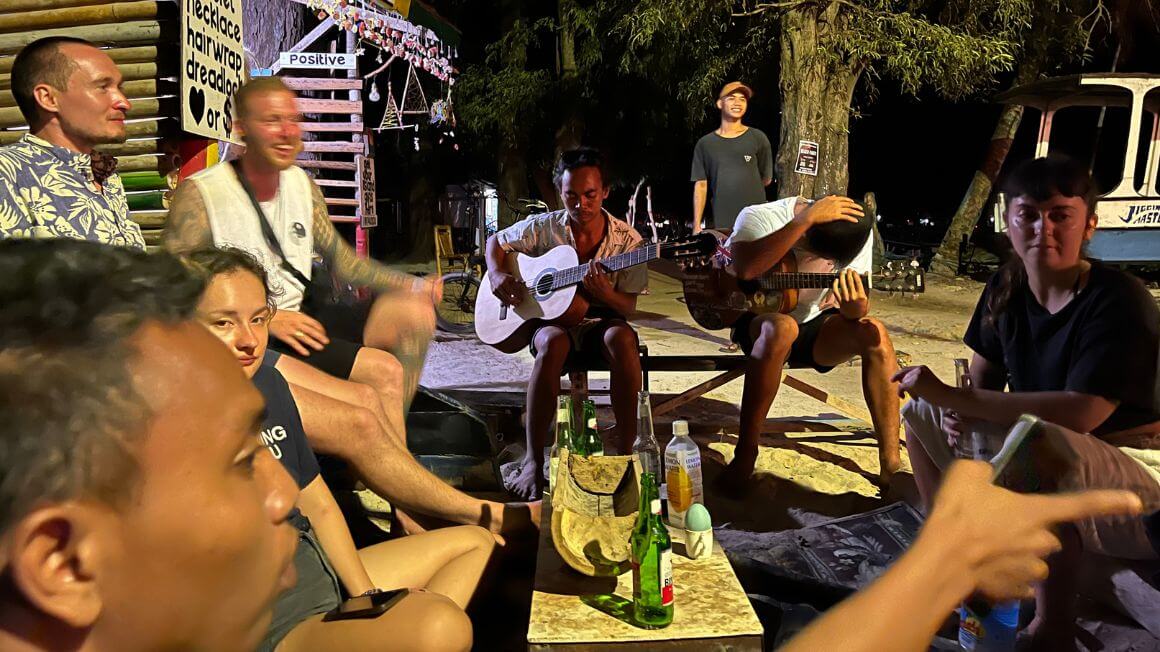 a group of travellers gather with some drinks jamming and playing music near the harbour in gili air, indonesia