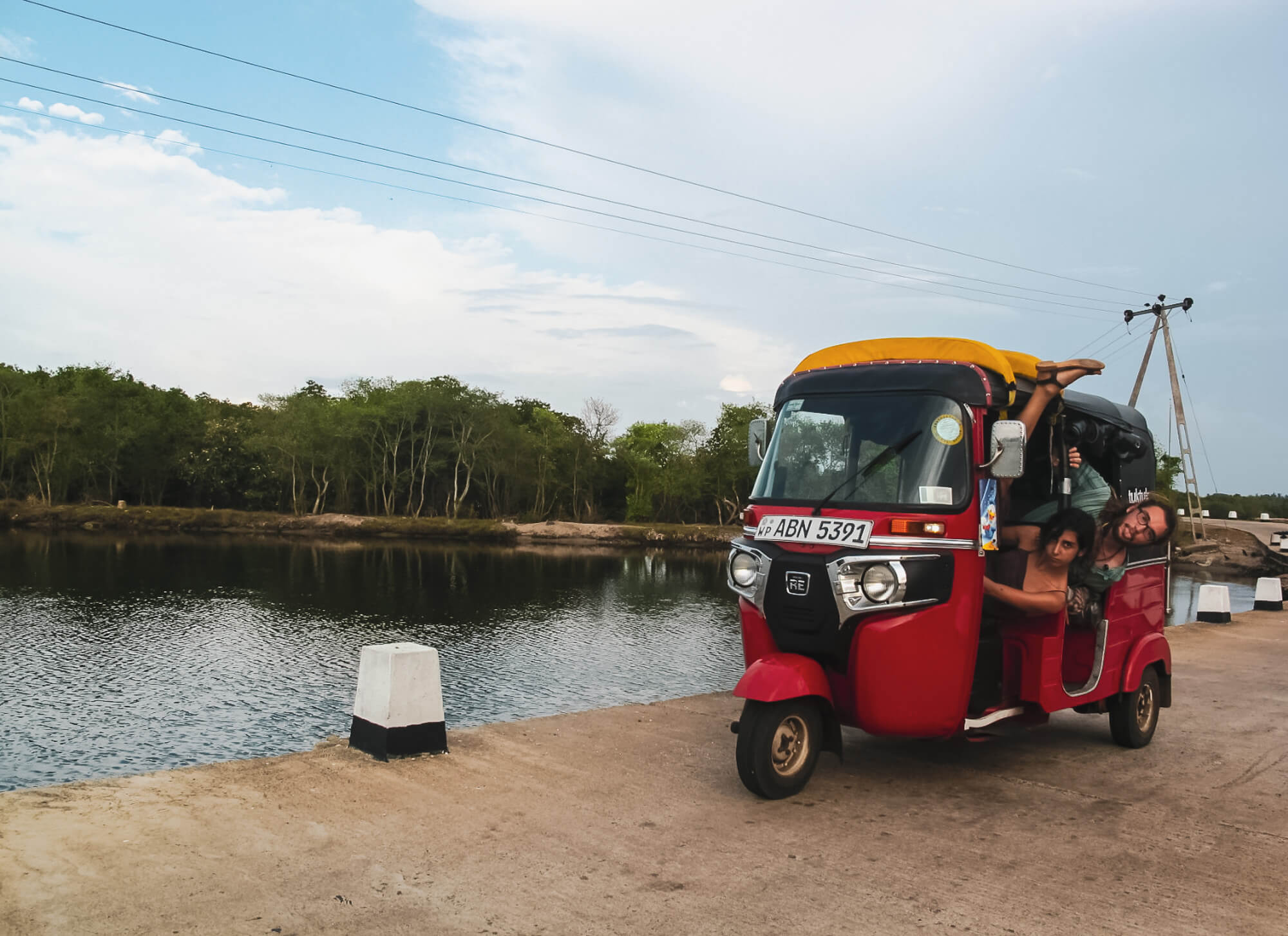 people goofing around inside a tuk tuk next to a river in sri lanka