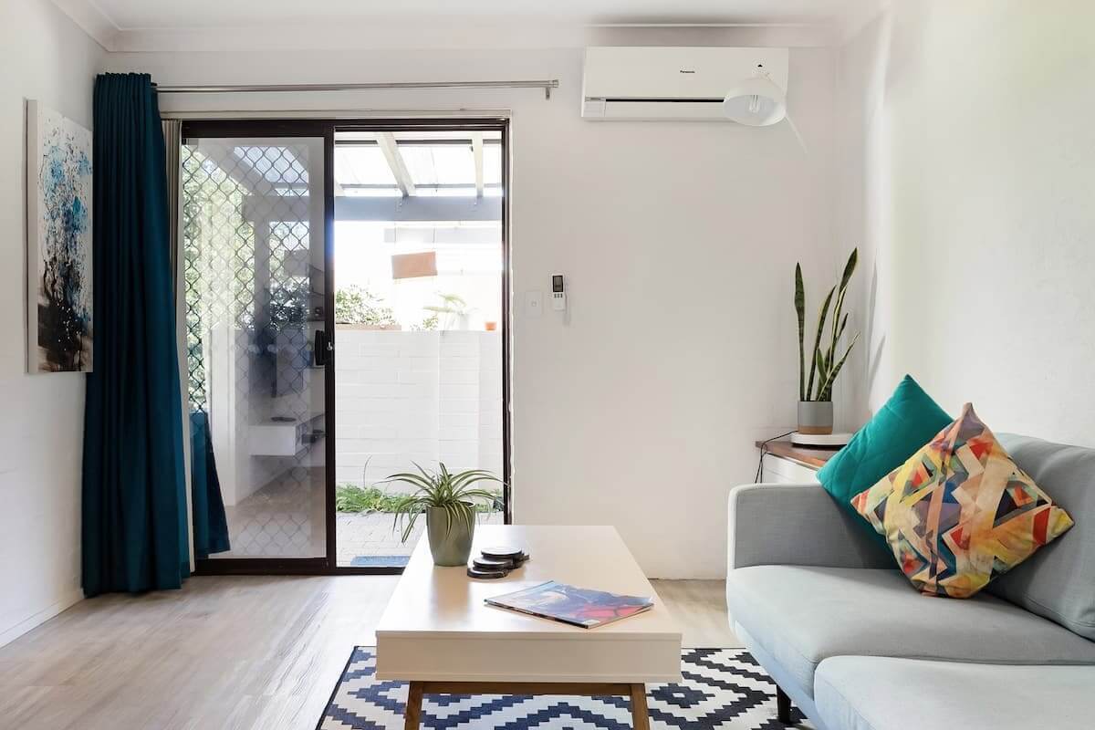 Modern, sleek lounge area with a sofa, coffee table, air conditioning unit and sliding front door. 