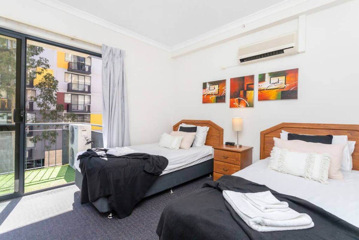 Twin bedroom with two single beds, air conditioning unit and sliding door onto the balcony. 