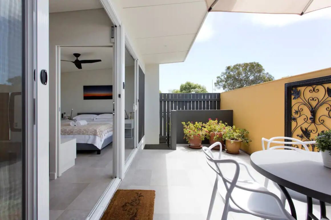 View of patio with dining table and plants and bed room inside sliding doors.