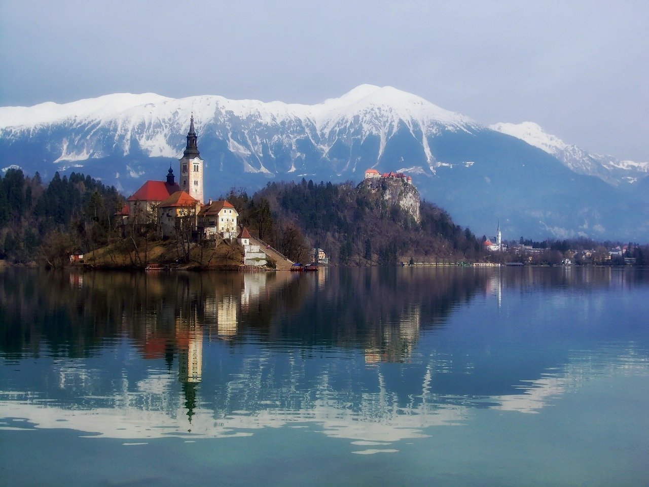 Snow capped mountains rise above a cathedral and some water in the Balkans. 