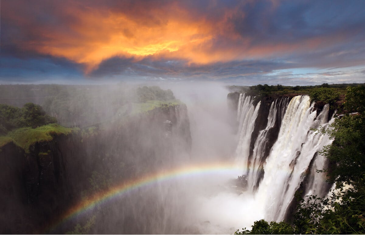 one of the most amazing waterfalls in the world with a rainbow and an orange sunset