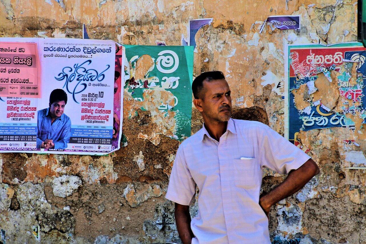 A Sri Lankan man stands in a street in front of Sinhalese posters