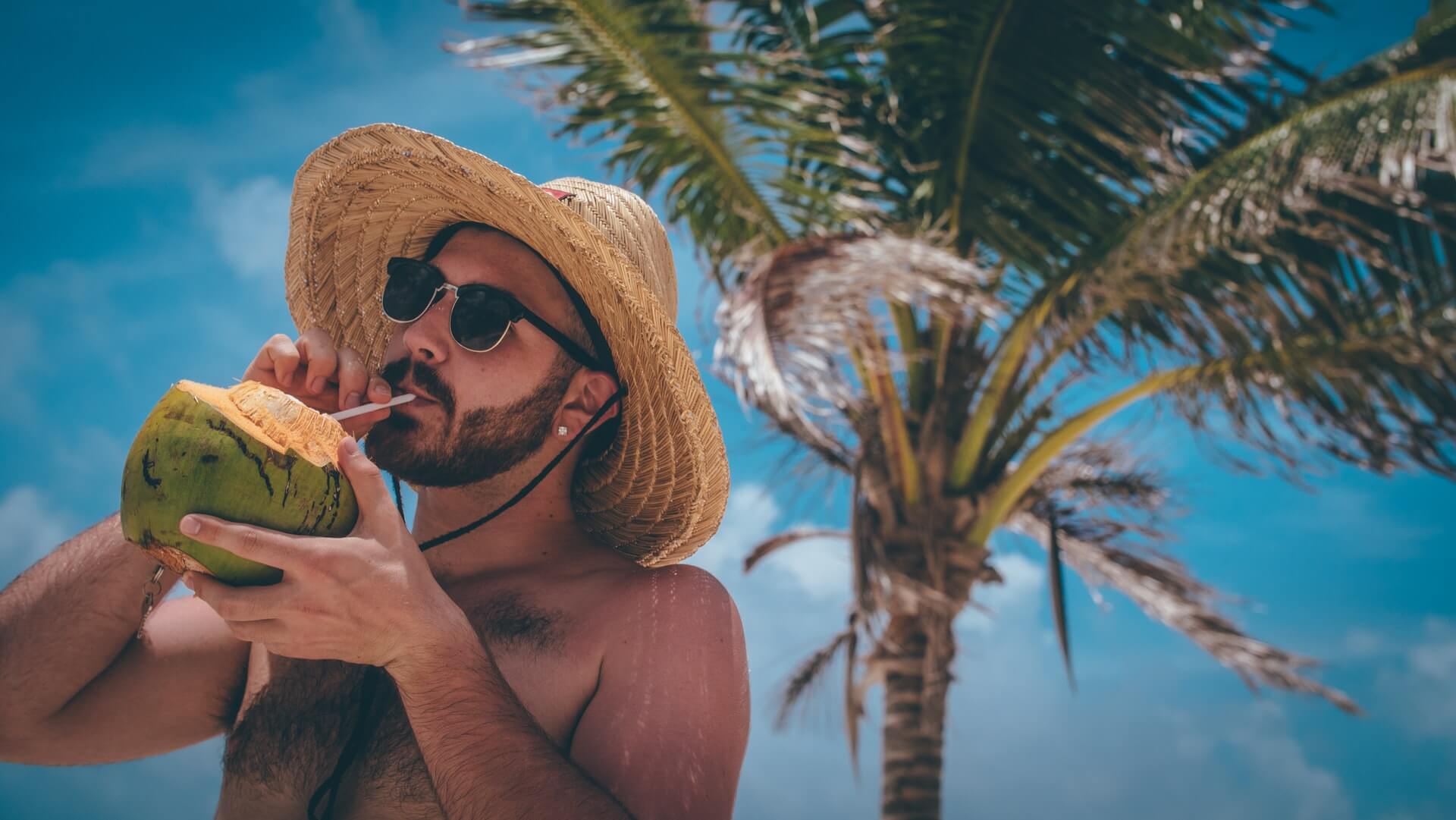 A man on vacation on a tropical island drinks from a coconut