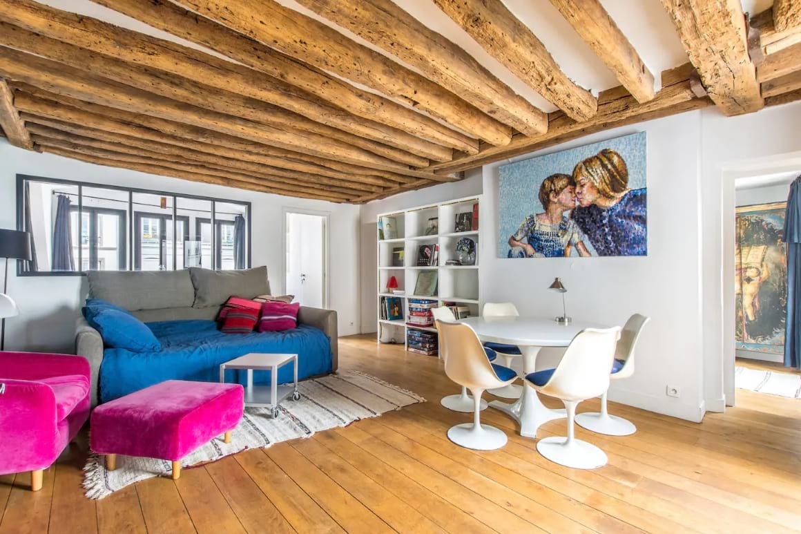 Living area with a wooden roof and floor. Comfy couches, dining table and art on the wall. 