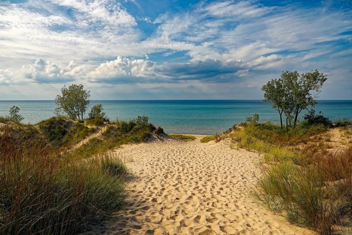 golden sand beach entrance through sand dunes toward blue sea in Michigan, USA