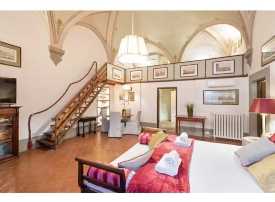 Spacious bedroom in the Airbnb with a tv, bed, table and chairs. You can see the staircase against the wall going up to the second floor.