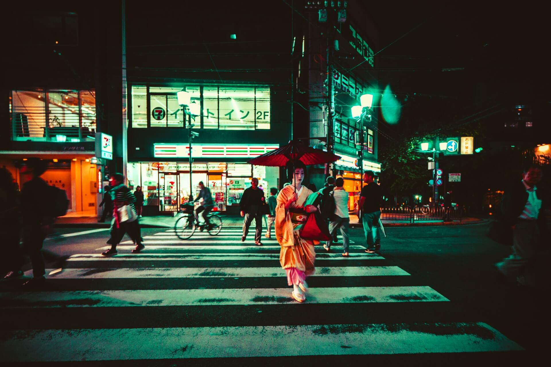 A geish in Kyoto crosses that street at night in front of a konbini