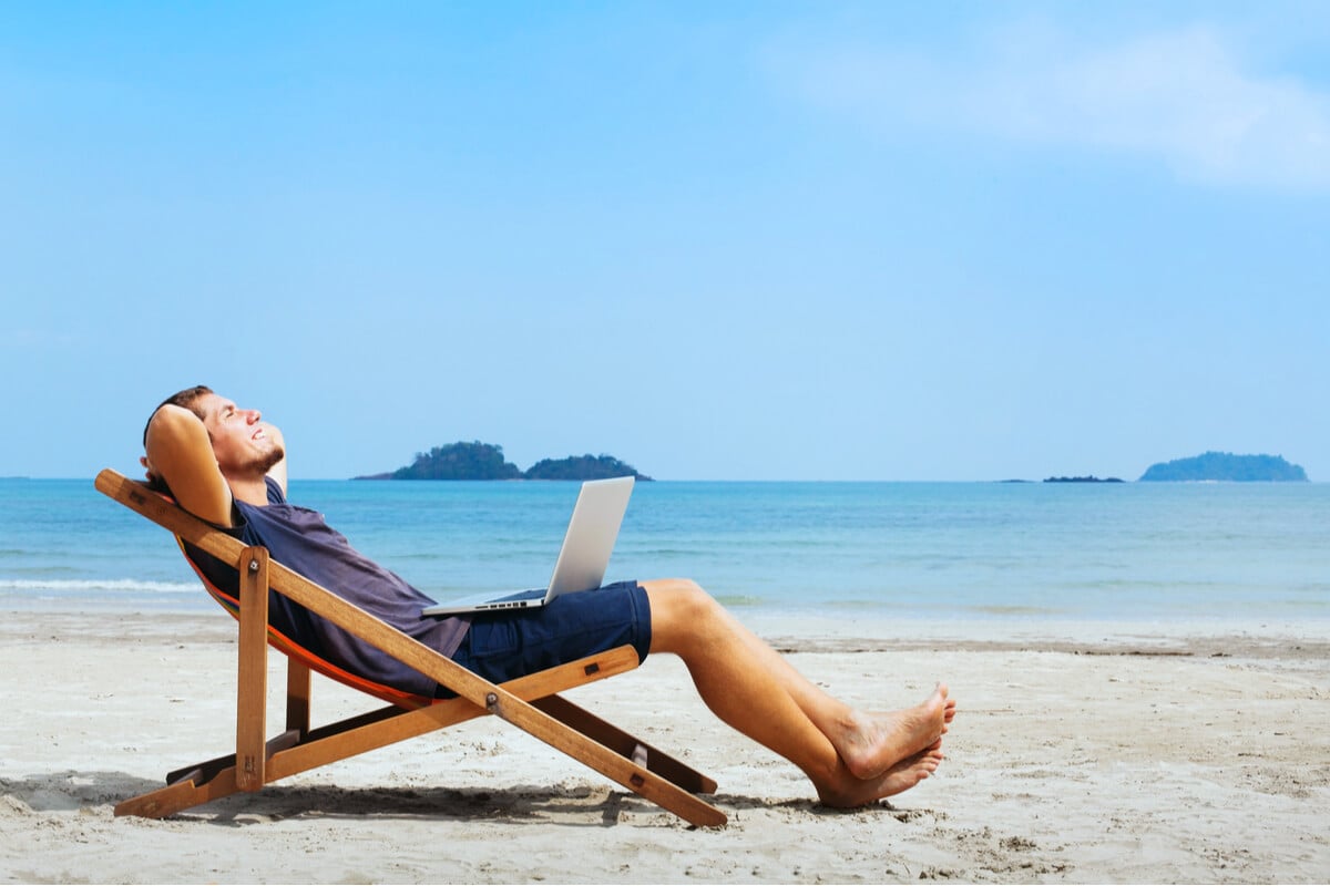 man sitting on tropical beach with laptop