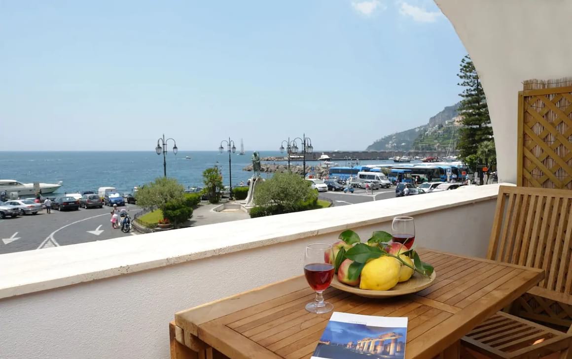 View of the balcony with wooden table and chairs. Looking over the balcony and onto the road and out to the ocean