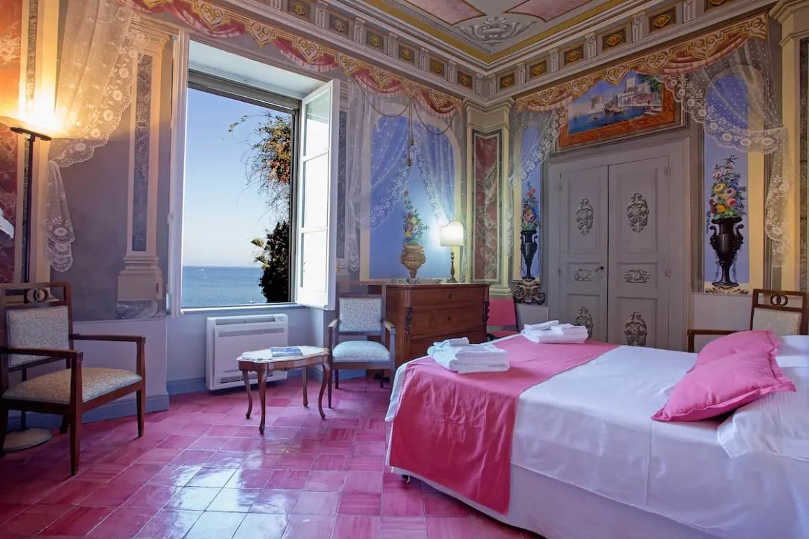 Faux-renaissance bedroom full of beautiful colour with a large window looking out to sea