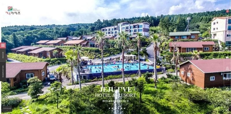 Jeju I've Hotel and Resort Jeju Island - an aerial picture of the hotel showing the pool, plam trees and lush green trees behind the accomodation