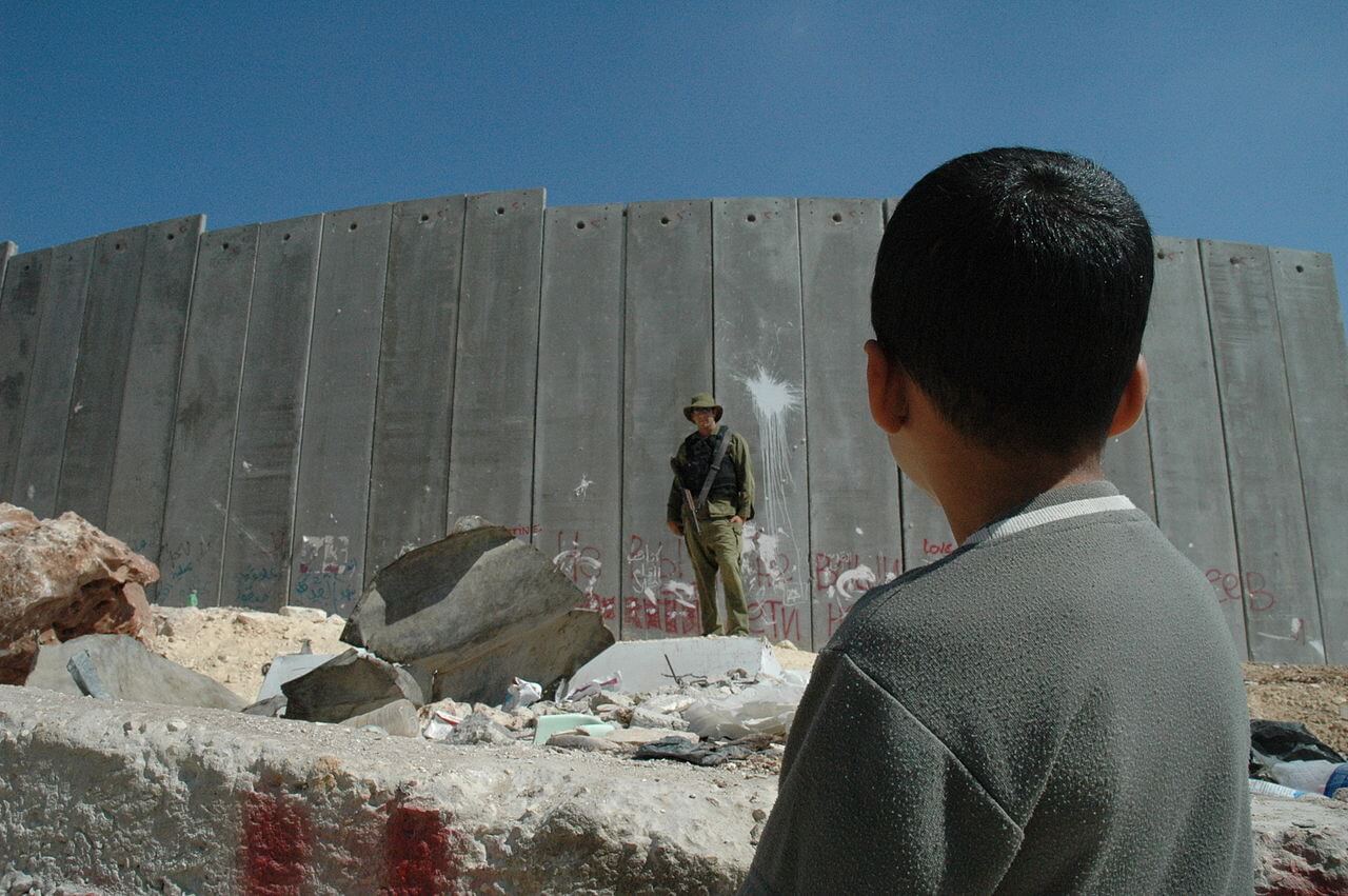 A Palestinian boy and Israeli soldier stand in front of the Israeli West Bank Barrier