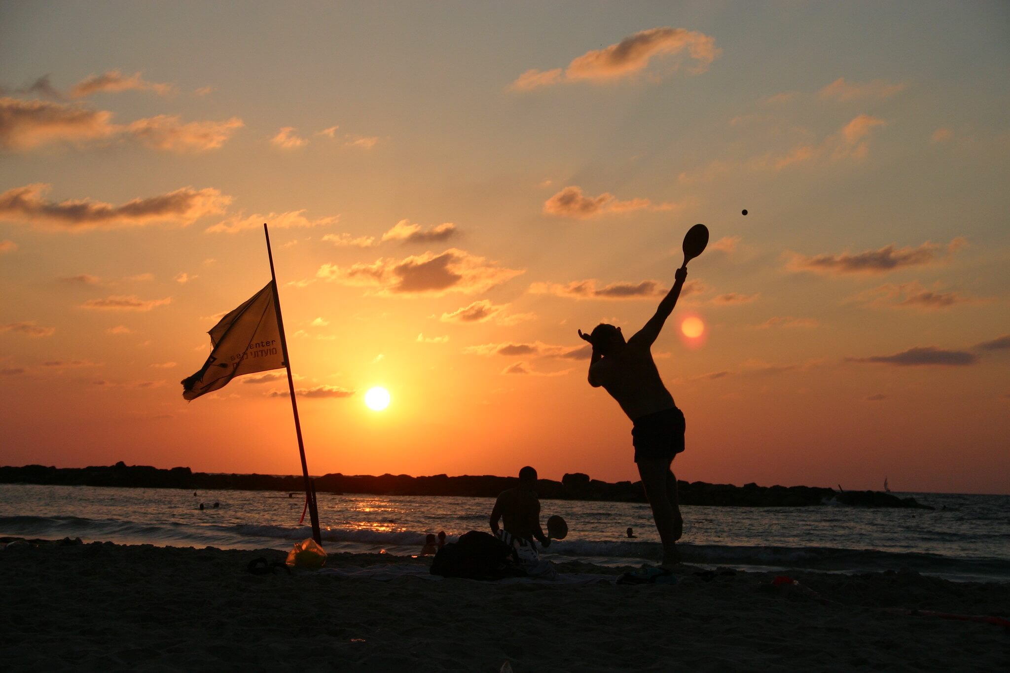 A man playing matkot on a beach in Tel Aviv at sunset