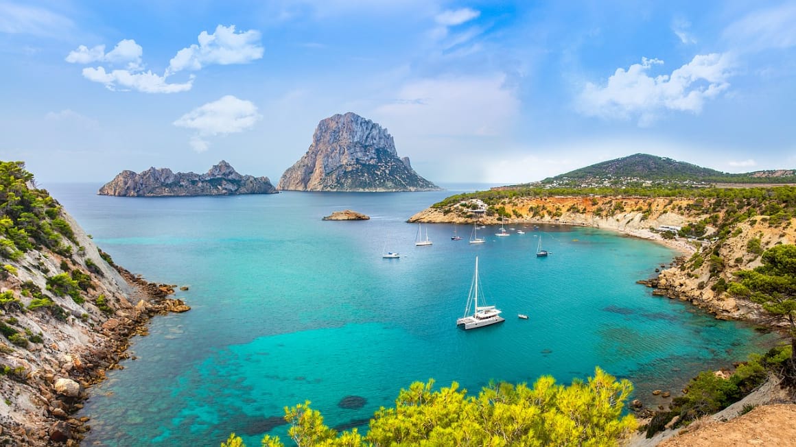 An aerial view of Ibiza's shoreline in Spain, with rock formations and boats adrift on the water.