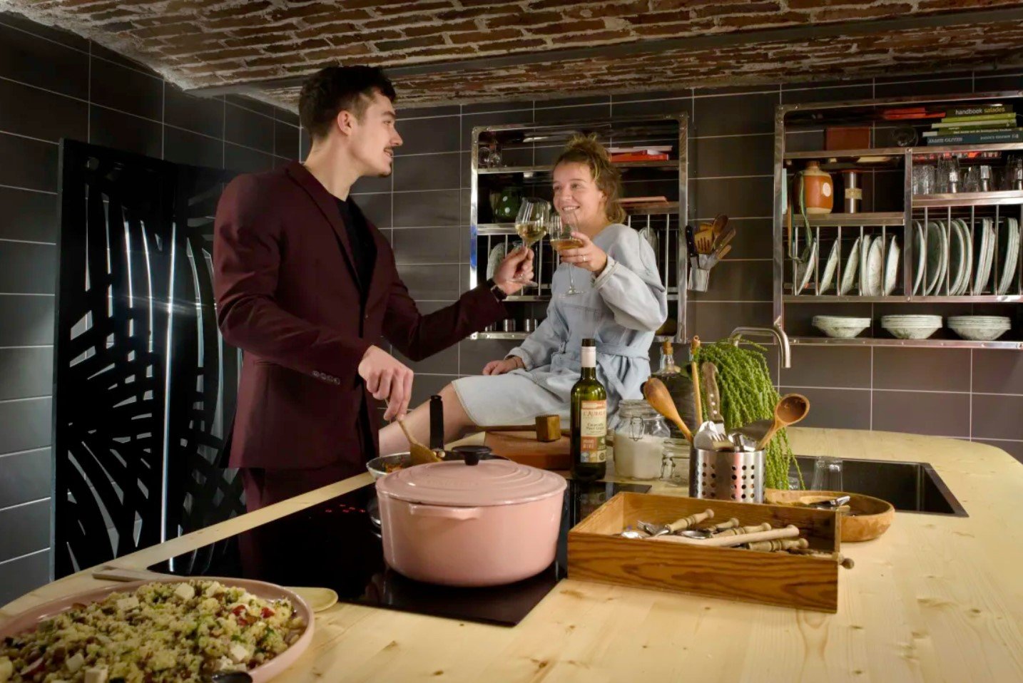 A hostel kitchen looking mighty fine with two travelers cooking