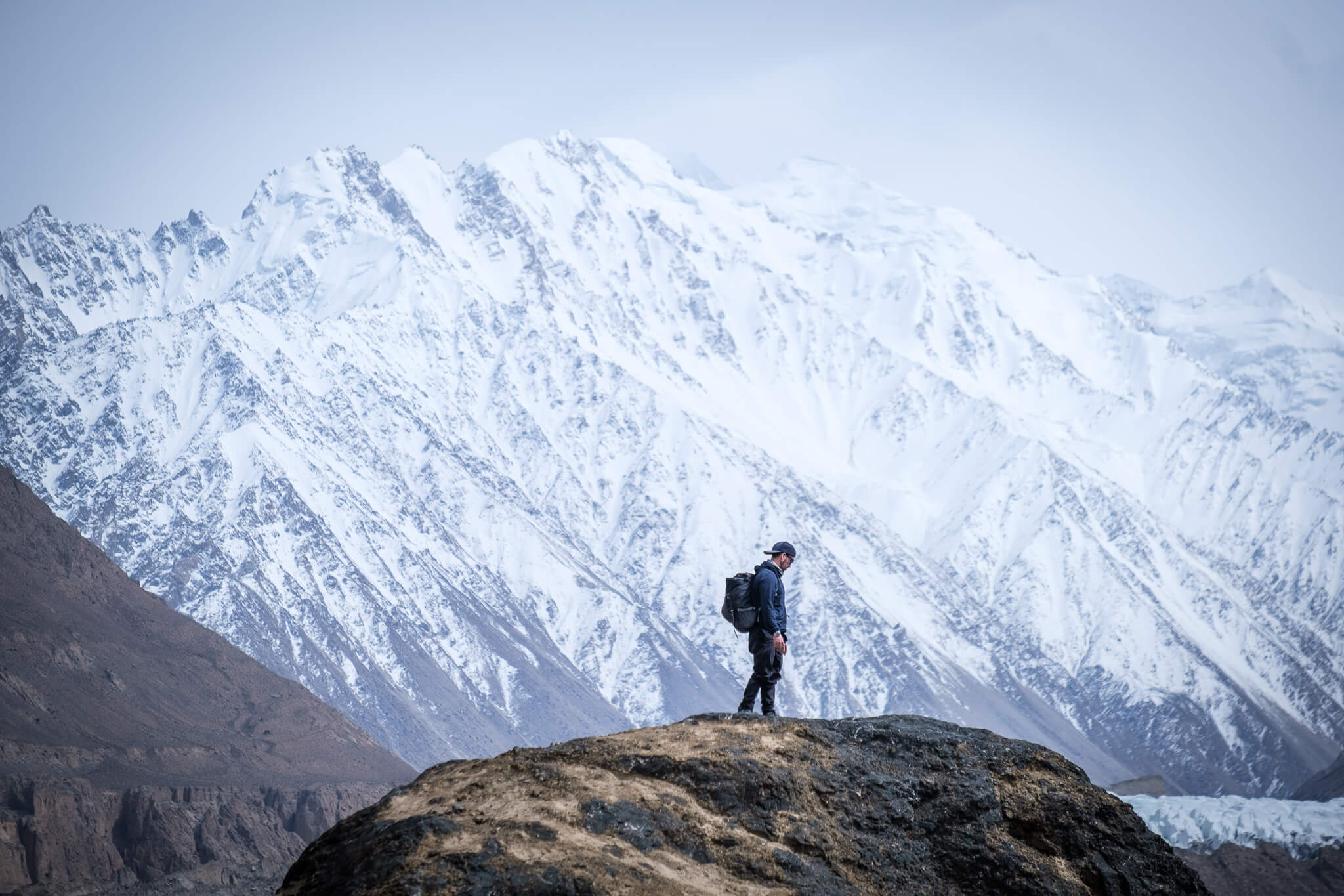 Will standing on a boulder with an icy mountain behind him in Pakistan