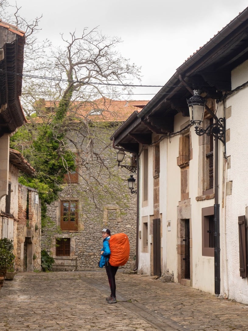 gilr between old houses carrying a huge backpack