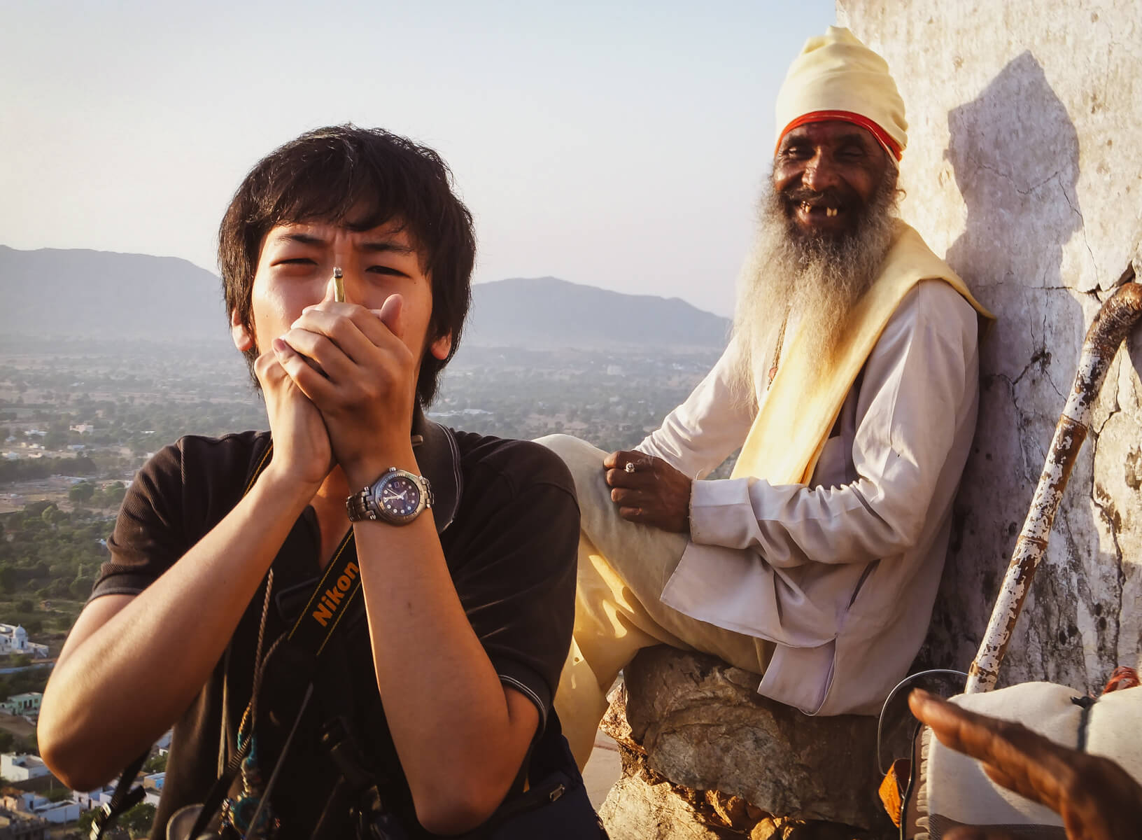 man smoking a joint with a sadhu looking on in india