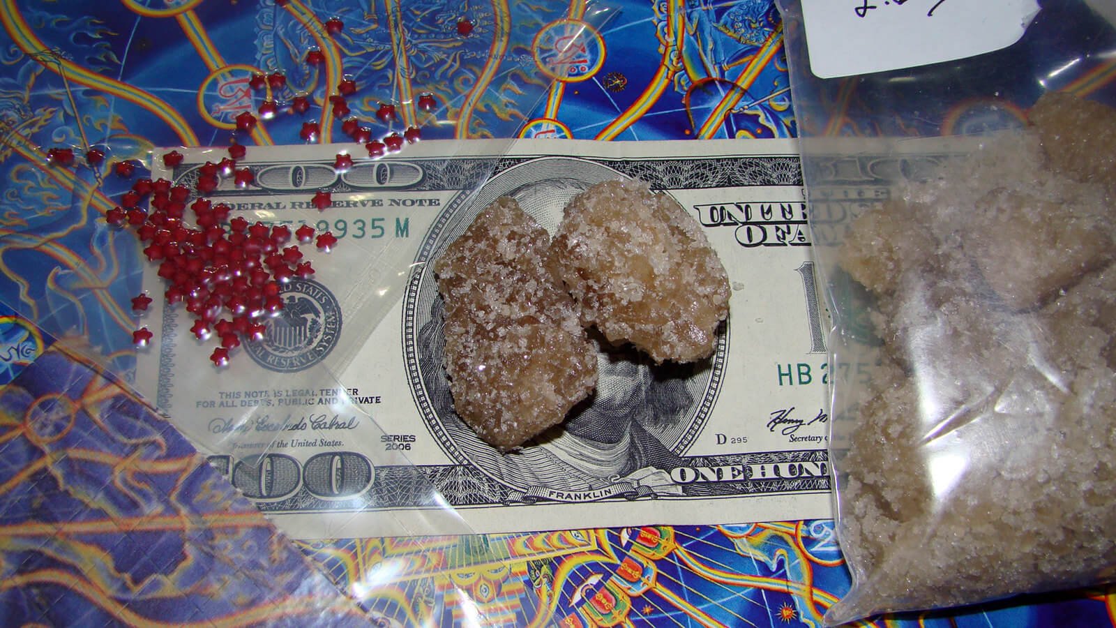 Drugs bought on the road - MDMA crystals and some LSD microdots sitting on top of a 100 USD bill