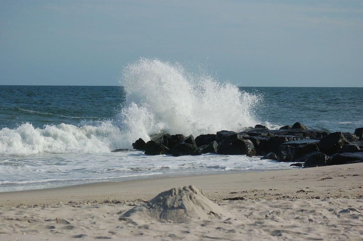 water breaking on rocks in front of the sandy shore at Cape May’s Beachfront