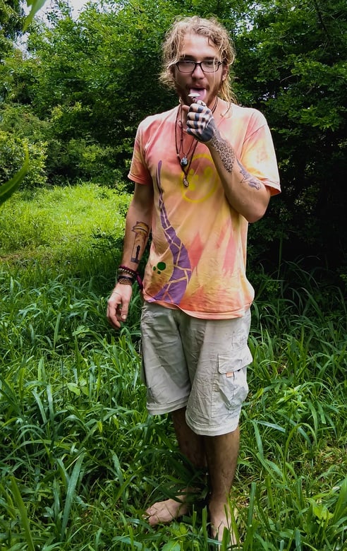 Ziggy standing in a forest eating ice cream showing his travel tattoos