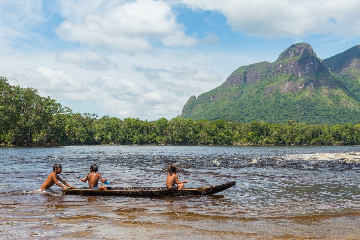 Local boys paddling a canoe beneath a mountain in Venezuela