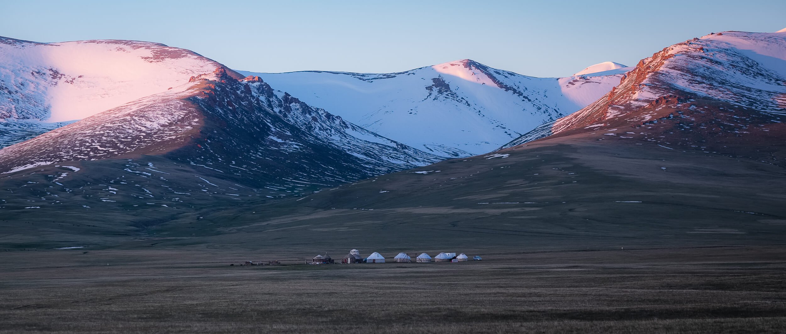 Yurts on a flat backdropped by snowcapped mountains in Kyrgyzstan - - next undiscovered holiday destination